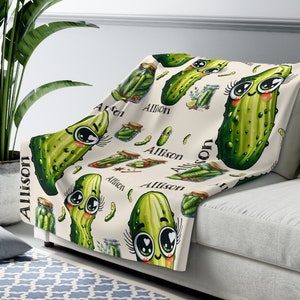 May include: A cream-colored fleece throw blanket with a repeating pattern of green cartoon pickles with big eyes and eyelashes. The name "Allison" is repeated throughout the pattern.