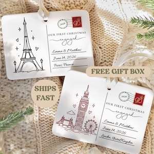 May include: Two rectangular white ornaments with ribbon loops. One features a black Eiffel Tower illustration, the other a red Big Ben and London Eye design. Both include the text "OUR FIRST CHRISTMAS engaged", "Emma & Matthew", "June 14, 2026", and a stamp graphic.