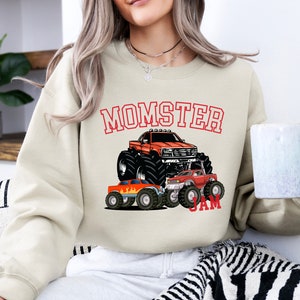 May include: A beige sweatshirt with a graphic of monster trucks and the text "Momster Jam".