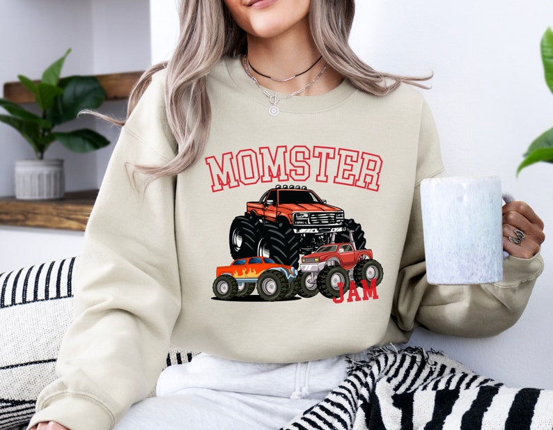 May include: A beige sweatshirt with a graphic of monster trucks and the text "Momster Jam".