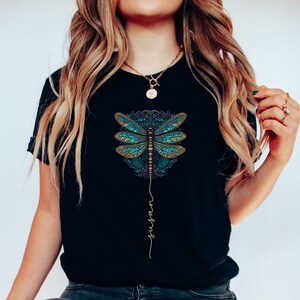 May include: Black t-shirt featuring a blue and gold dragonfly graphic with the word "surrender" written vertically beneath it.