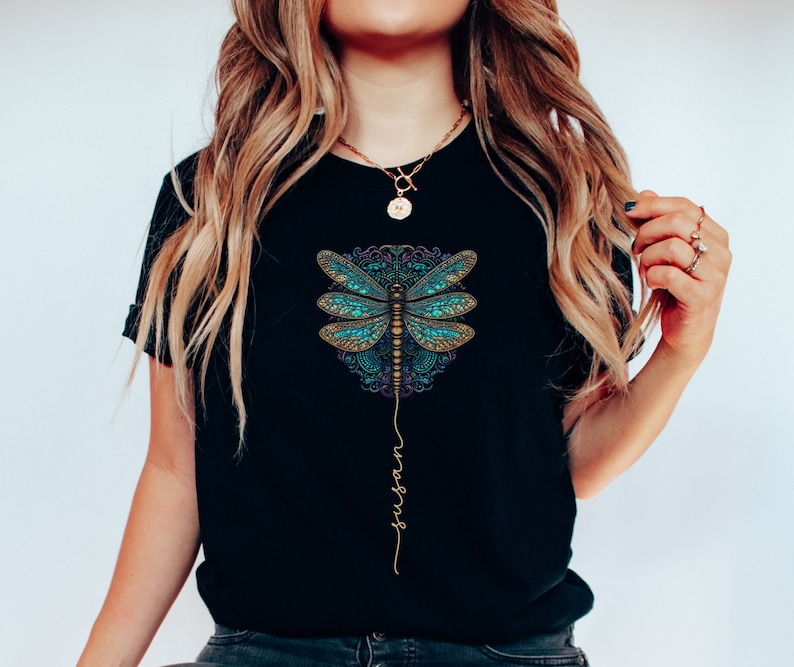 May include: Black t-shirt featuring a blue and gold dragonfly graphic with the word "surrender" written vertically beneath it.