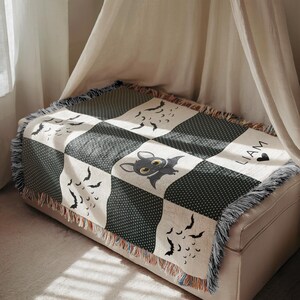 May include: A black and white throw blanket with a bat and bat silhouettes design. The blanket has a checkerboard pattern with a fringe trim. The name "LIAM" is printed on the blanket.