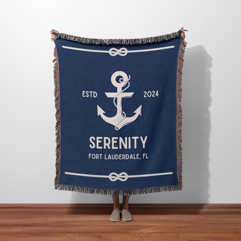 May include: A navy blue woven throw blanket featuring a large white anchor graphic wrapped in rope. The text reads ESTD 2024, SERENITY, and FORT LAUDERDALE, FL. The blanket has a decorative fringe on the top and bottom edges and horizontal rope borders.