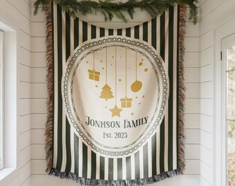 May include: A green and white striped throw blanket with a circular design featuring Christmas ornaments and the text "JOHNSON FAMILY Est. 2023." The blanket has a fringed edge and is decorated with a garland.