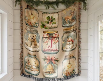 May include: A beige throw blanket featuring nine decorative jars with winter-themed illustrations. The jars contain images of a star, holly, a deer, a polar bear, a snowman, a church, a bell, and floral arrangements. The word "JOHNSONS" is printed on one jar.
