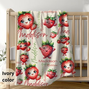 May include: A cream-colored baby blanket with a repeating pattern of red strawberries with happy faces and green leaves. The name "Maddison" is written in a cursive font throughout the blanket.