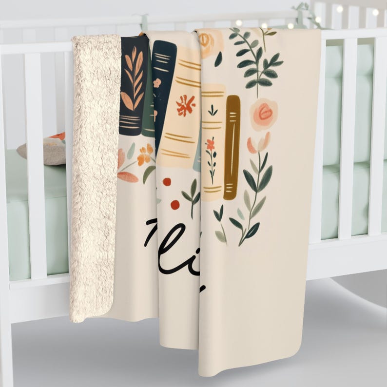 May include: A cream-colored throw blanket with a floral design featuring stacked books, leaves, and flowers. The text "Read" is written in black cursive on the blanket.