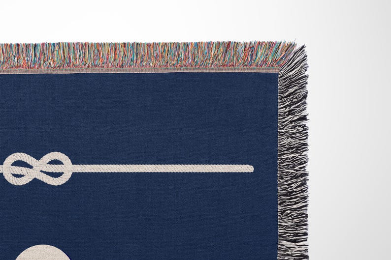 May include: A dark navy blue woven throw blanket featuring a white rope graphic tied in a knot. The blanket has a decorative fringe edge with multicoloured threads woven into the top border and solid black fringe along the side edge.