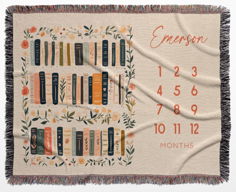 Op de afbeelding: Beige geweven sprei met een boekenplankontwerp en bloemaccenten. De sprei heeft een boekenplankillustratie met verschillende kleuren boeken en de naam "Emerson" in een scriptlettertype. Cijfers 1-12 worden weergegeven voor maandelijkse foto's.