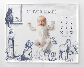 May include: A white baby milestone blanket with a navy blue farm animal illustration. The blanket features the name "Oliver James" and numbers for tracking baby's age in months. A baby in a striped onesie is lying on the blanket.