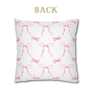 Puede incluir: Almohada blanca con un patr&oacute;n de lazos rosas. La parte posterior de la almohada tiene la palabra "BACK" impresa.
