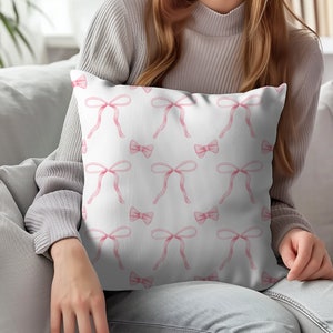 Puede incluir: Una almohada blanca con un patr&oacute;n de lazo de acuarela rosa. La almohada es suave y c&oacute;moda, y el patr&oacute;n es sutil y elegante.