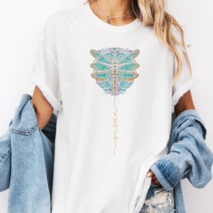 May include: White t-shirt featuring a blue and gold dragonfly design with the words "fly high" written in gold script.