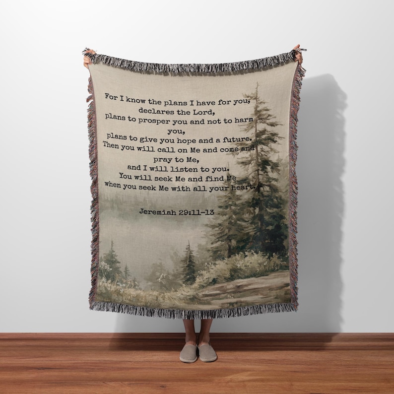 Puede incluir: Una manta tejida con una escena de bosque y texto de Jerem&iacute;as 29:11-13. La manta tiene un borde con flecos y una paleta de colores neutros con tonos beige, marr&oacute;n y verde. El texto est&aacute; en una fuente oscura.