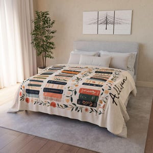 May include: A cream-colored fleece blanket with a personalized name "Allison" in black script. The blanket features a pattern of stacked books with floral accents in shades of orange, green, blue, and pink.