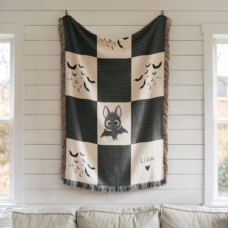 May include: A black and cream-colored throw blanket with a bat theme. The blanket features a checkerboard pattern with black polka dots and bat silhouettes. A central square showcases a cute bat illustration with the name "LIAM" and a heart symbol.