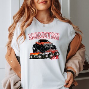 May include: White t-shirt with a red graphic of a monster truck and the text "MOMSTER JAM".
