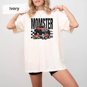 May include: A white t-shirt with the text "MOMSTER JAM" printed in black. The design features a cartoon monster truck with flames and chequered flags.