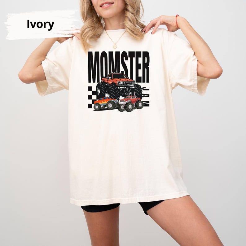 May include: A white t-shirt with the text "MOMSTER JAM" printed in black. The design features a cartoon monster truck with flames and chequered flags.