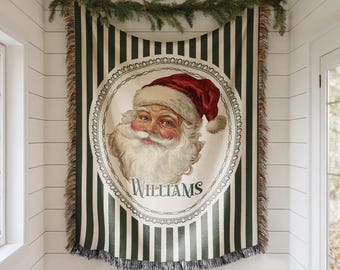 May include: A Christmas-themed tapestry with a portrait of Santa Claus in a red hat and white beard, framed by a decorative oval. The tapestry has green and white vertical stripes and the name "Williams" is printed below the portrait.