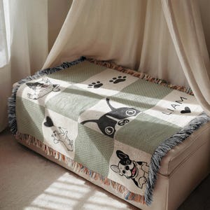 May include: A woven throw blanket featuring a patchwork design with images of French Bulldogs, paw prints, and the name "LIAM". The blanket has a fringed edge and a color palette of white, green, and black.