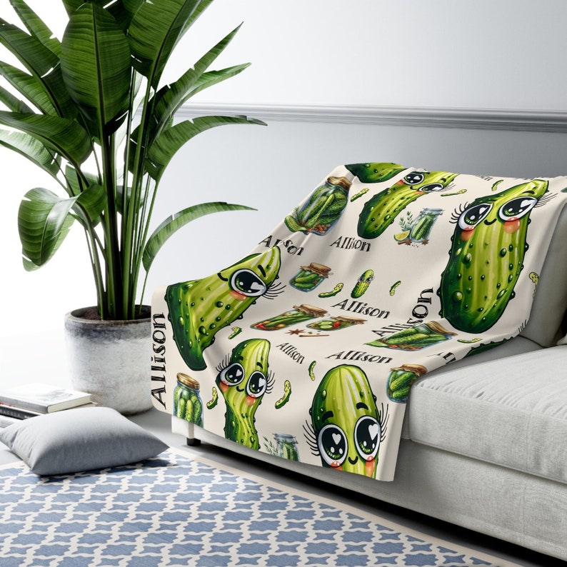 May include: A cream-colored fleece throw blanket with a repeating pattern of green cartoon pickles with big eyes and eyelashes. The name "Allison" is repeated throughout the pattern.