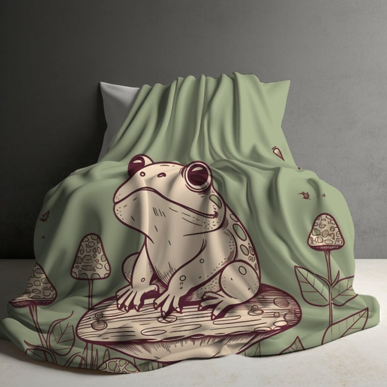 May include: A green throw blanket with a cartoon frog sitting on a mushroom. The frog is brown with white spots and has a green background.