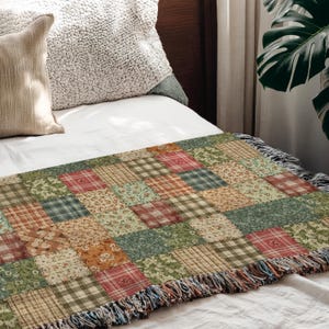 May include: A patchwork throw blanket with a variety of patterns and colors, including plaid, floral, and solid squares in shades of green, red, and tan. The blanket has a fringed edge and is placed on a white bed.