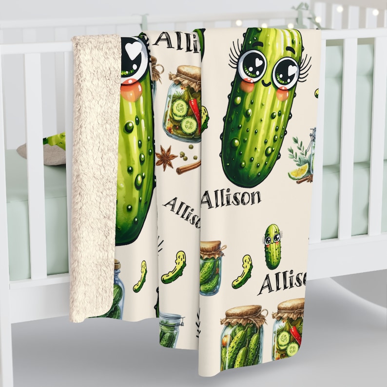 May include: A cream-colored fleece blanket with a repeating pattern of green pickles, jars of pickles, and spices. The name "Allison" is written in a cursive font on the blanket.