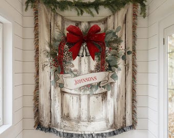 May include: A tapestry featuring a distressed white door design, adorned with a red bow, pinecones, and greenery. The banner reads "JOHNSONS". The tapestry is fringed and decorated with a garland of evergreen branches.