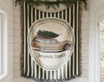 May include: A woven throw blanket with a vintage car carrying a Christmas tree on top. The car is inside a circular design with the text "JONHSON FAMILY". The blanket has green and white vertical stripes with fringed edges and is decorated with a garland.