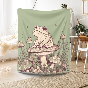 May include: A green tapestry featuring a cartoon frog sitting on a mushroom with other mushrooms and foliage surrounding it.