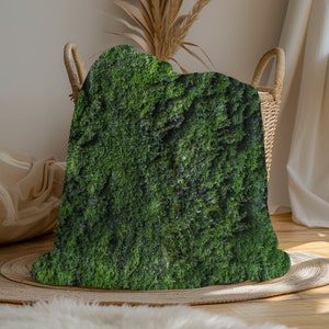 May include: A green moss-covered throw blanket with a soft, fuzzy texture. The blanket is draped over a wicker basket.