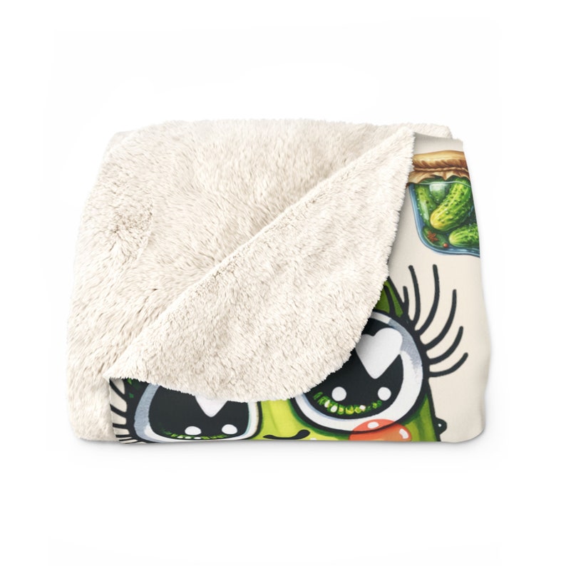 May include: A plush throw blanket with a cartoon pickle design. The pickle has large eyes, eyelashes, and a heart-shaped pupil. The pickle is green and has a red blush on its cheek. There is a jar of pickles in the background.