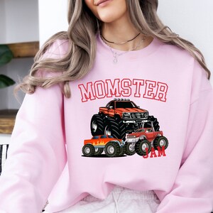 May include: Pink sweatshirt with a graphic of monster trucks and the text "MOMSTER JAM".