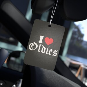 May include: Black car air freshener with white text that says "I ♥ Oldies".