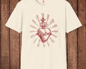 Könnte beinhalten: Cremefarbenes T-Shirt mit roter Grafik eines Herzens mit Dornenkrone, Kreuz und Strahlen. Das Design befindet sich mittig auf der Vorderseite des kurzärmeligen Shirts. Das Shirt hat einen Rundhalsausschnitt und ein kleines Logo am Ausschnitt.