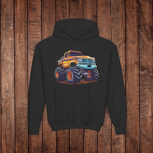 May include: Black hoodie featuring a vibrant illustration of an orange and yellow monster truck with oversized tires. The truck has a blue front grill and is set against a brown background. The design is centered on the front of the hoodie.