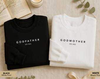 Può includere: Due felpe, una nera e una bianca. La felpa nera ha la scritta "GODFATHER EST. 2025" stampata in bianco. La felpa bianca ha la scritta "GODMOTHER EST. 2025" stampata in nero. Su sfondo neutro.