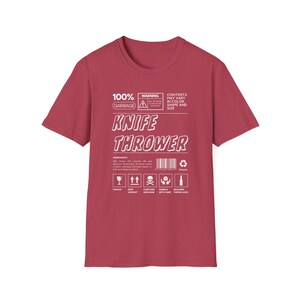 May include: Red t-shirt featuring a white graphic of a warning label that reads "100% Garbage" and "Knife Thrower". The label includes a warning symbol and a barcode.