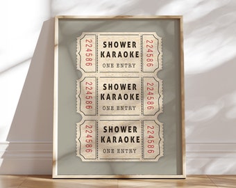 May include: A framed print featuring three vintage-style tickets. Each ticket reads "SHOWER KARAOKE ONE ENTRY" in red text. The tickets have a cream background with a decorative border and the number "224586". The frame is a light brown color.