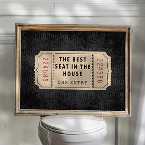 以下が含まれることがあります： 「The Best Seat in the House」と書いてある、ヴィンテージチケットのデザインの黒と白の額縁付きのサイン。両側に224586という番号が書かれている。サインは白いトイレの上に掛かっている。