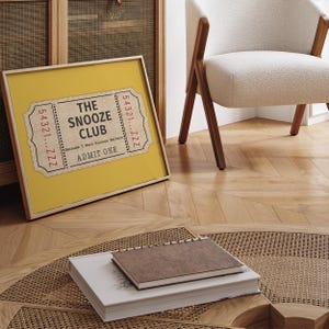 May include: A yellow framed print with a vintage ticket design. The ticket reads "The Snooze Club" and "Because 5 More Minutes Matters". The ticket also says "Admit One" and has a number "54321...ZZZ" on each side.