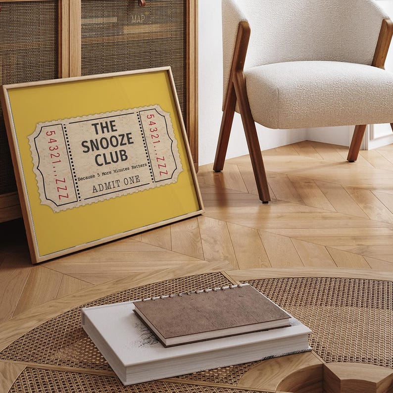 May include: A yellow framed print with a vintage ticket design. The ticket reads "The Snooze Club" and "Because 5 More Minutes Matters". The ticket also says "Admit One" and has a number "54321...ZZZ" on each side.