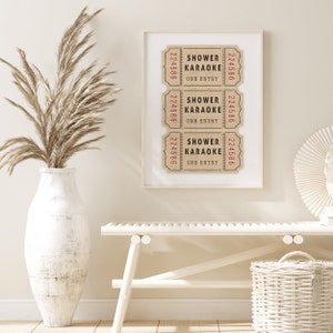 May include: Three brown paper tickets with the text "Shower Karaoke One Entry" and the number "224586" printed on them. The tickets are framed in a white frame and hung on a white wall.