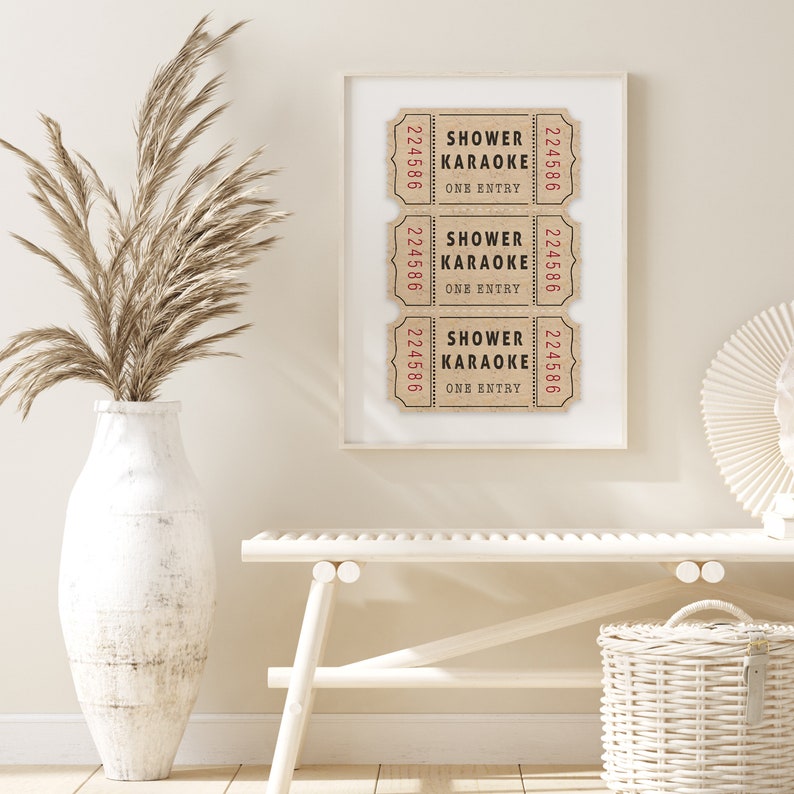 May include: Three brown paper tickets with the text "Shower Karaoke One Entry" and the number "224586" printed on them. The tickets are framed in a white frame and hung on a white wall.
