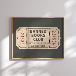 以下が含まれることがあります： 「Banned Books Club」という文字と「Defy, Read, Repeat, Admit One」という文字が書かれた、ヴィンテージチケットの額装されたプリント。チケットの両側に224586という番号が書かれている。