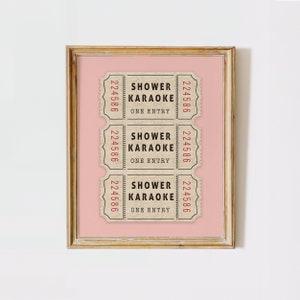 May include: Three vintage-style tickets with the text "Shower Karaoke" and "One Entry" printed on them. The tickets are brown with black text and red numbers. The tickets are framed on a pink background.