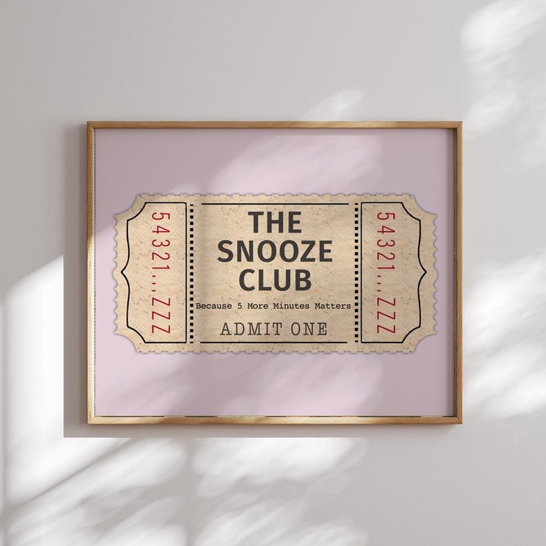 May include: A vintage-style ticket with the text "The Snooze Club" in black lettering on a beige background. The ticket has a red border and the text "Because 5 More Minutes Matters" and "Admit One" in red lettering.